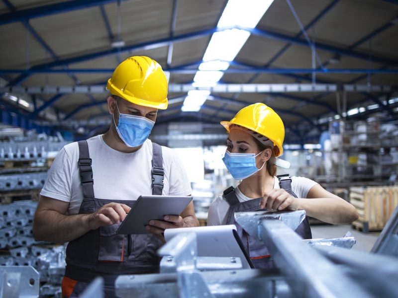 Industrial workers with face masks protected against corona virus discussing about production in factory.