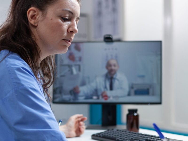 Therapist nurse discussing sickness diagnostic with remote doctor during online videocall meeting conference during clinical consultation in hospital office. Telemedicine call on computer screen